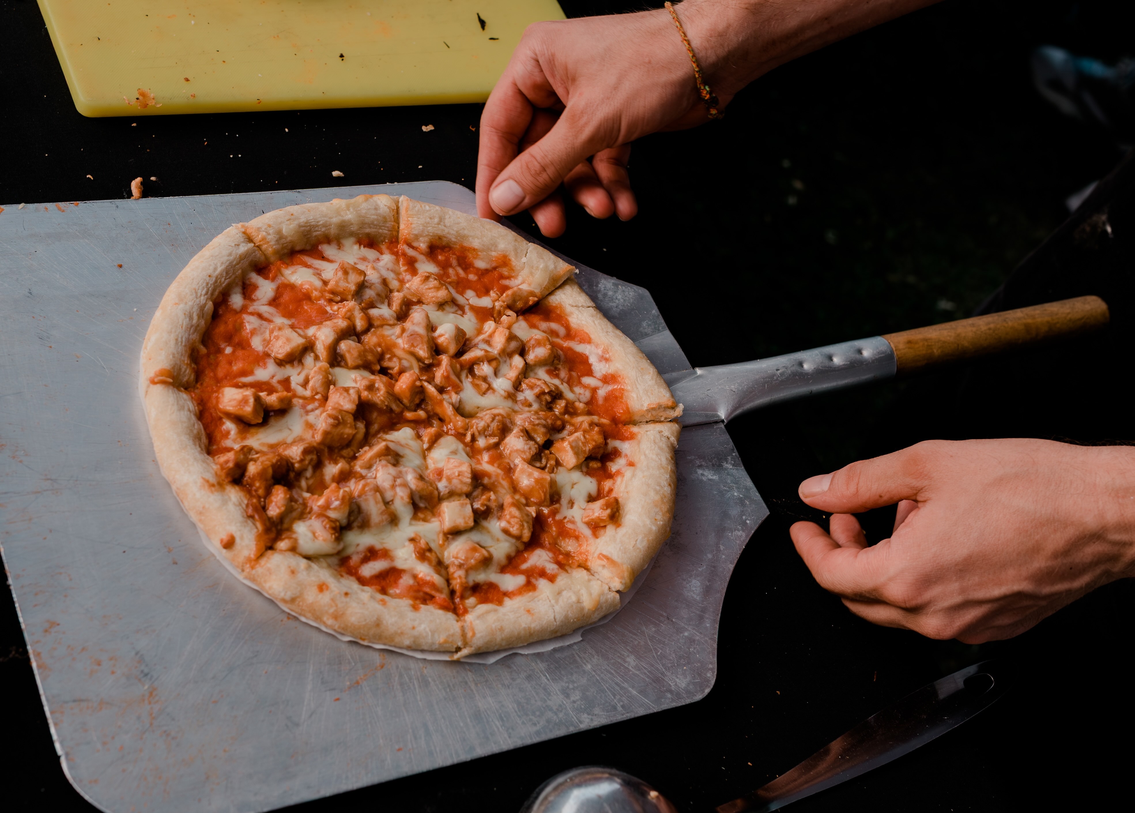 Fresh wood-fired pizza being served on a paddle at an event